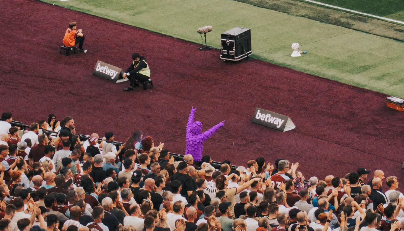 Purple Post-it man celebrating pitchside in front of a packed home stand
